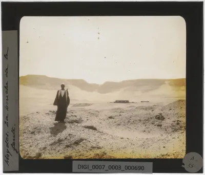 A man at Umm el-Qa'ab, Abydos, with the wadi access visible beyond. This quiet stretch of desert holds the burials of the earliest rulers of